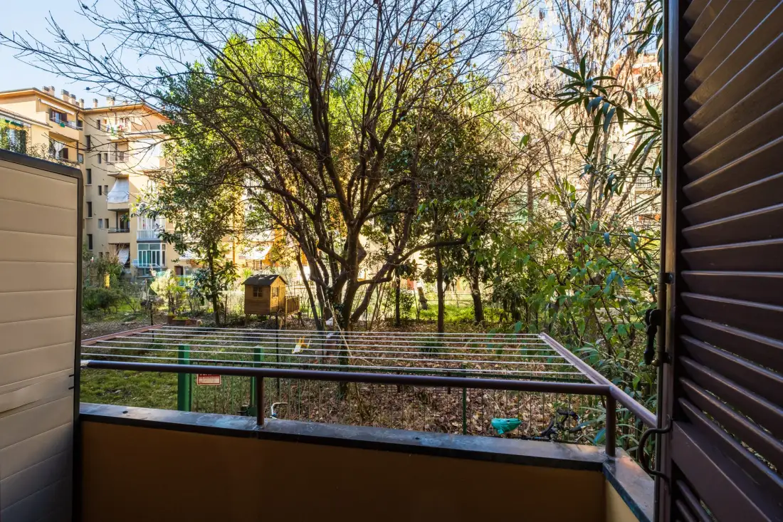 Un balcón da a un patio frondoso con árboles y edificios de apartamentos alrededor.