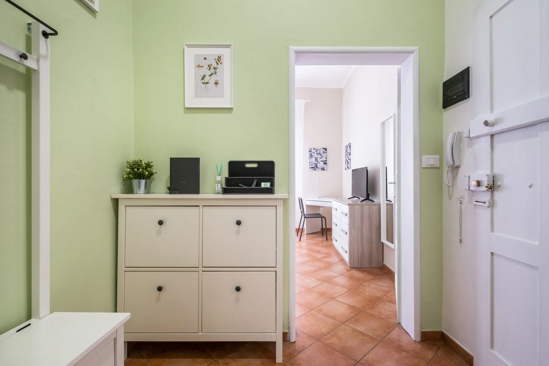 Una entrada verde pálido con un mueble crema y una puerta abierta a una habitación.