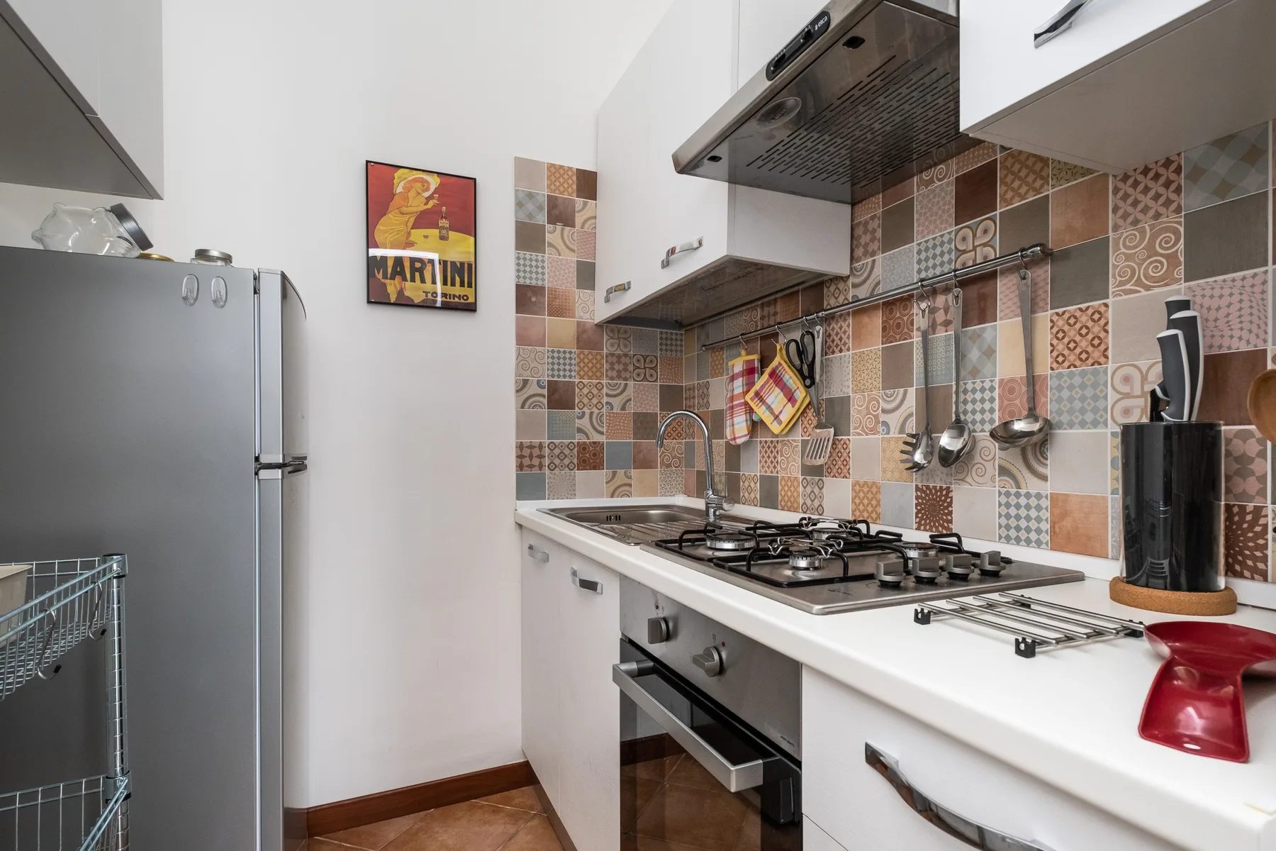 Una cocina compacta con estufa de gas, horno y salpicadero de azulejos estampados.