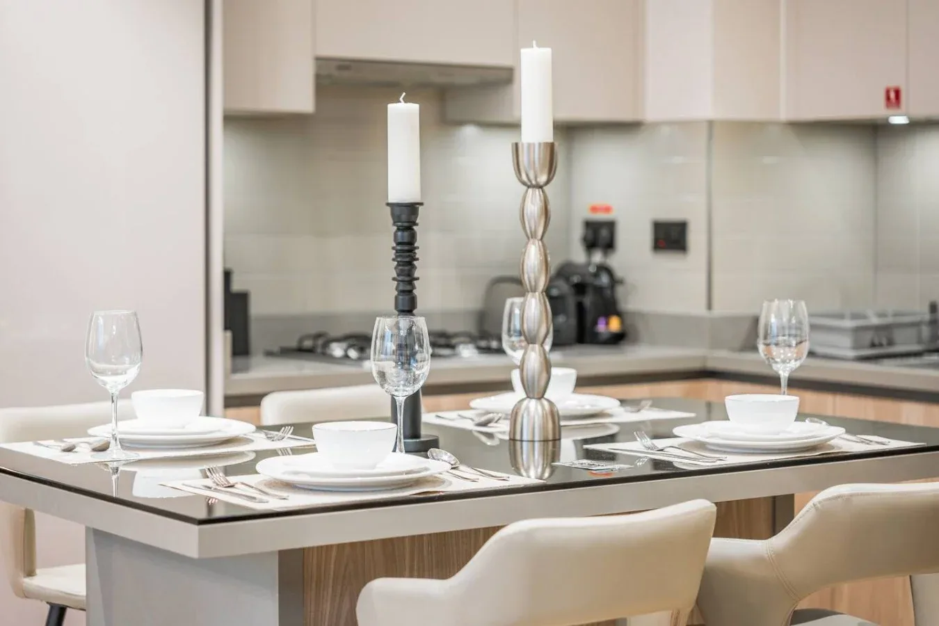 Una mesa de comedor está preparada con platos, copas y dos velas altas en una cocina.
