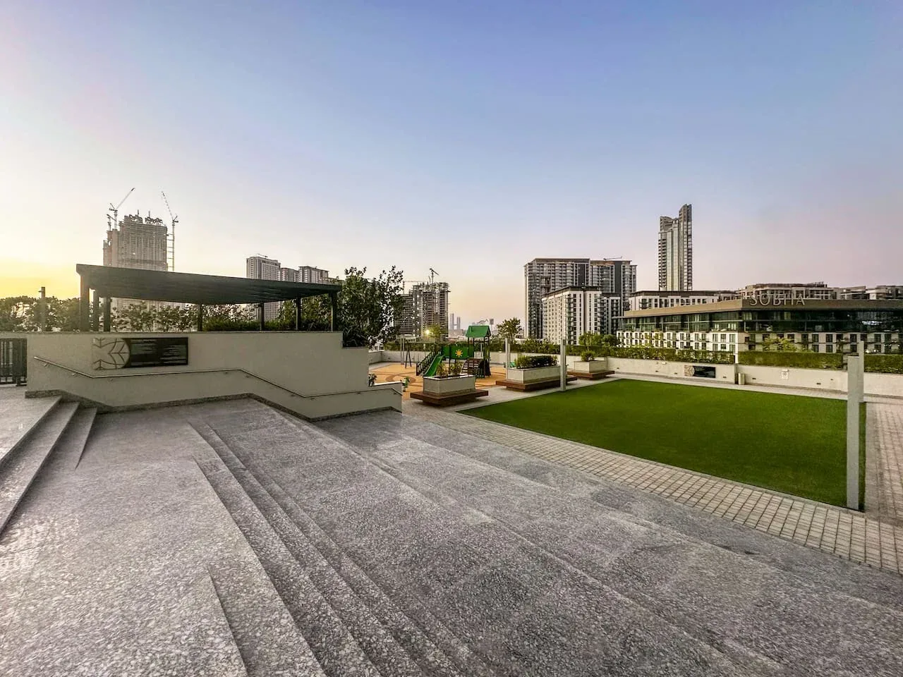 Una terraza en la azotea con amplios escalones pavimentados, césped verde y edificios de la ciudad al fondo.