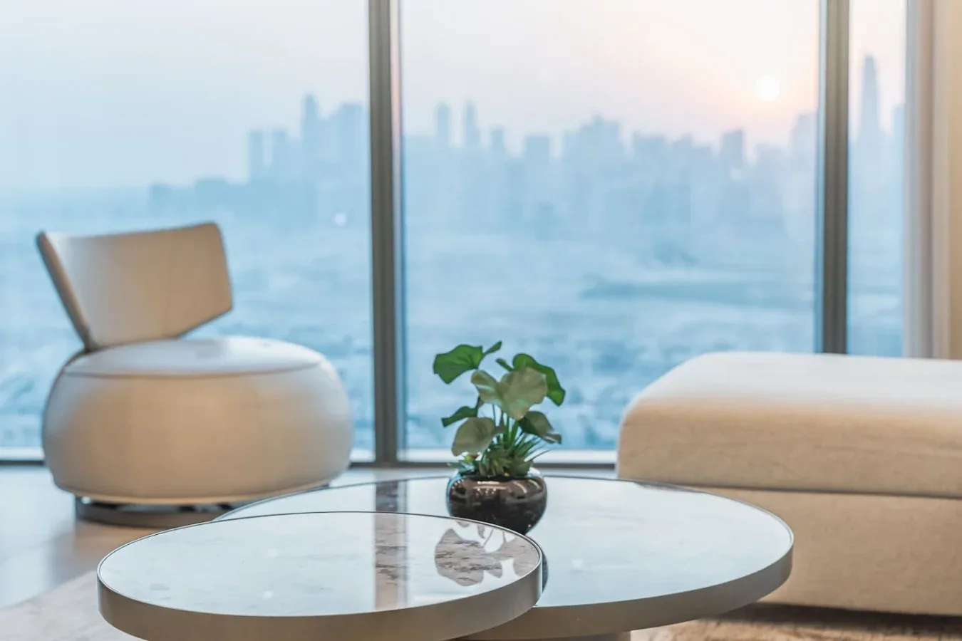 Una sala de estar moderna con asientos, una mesa de centro redonda y amplios ventanales con vista a la ciudad.