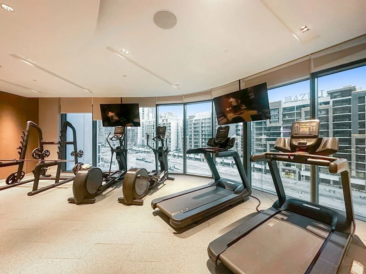 Un gimnasio luminoso con cintas de correr y equipos de ejercicio junto a grandes ventanales.