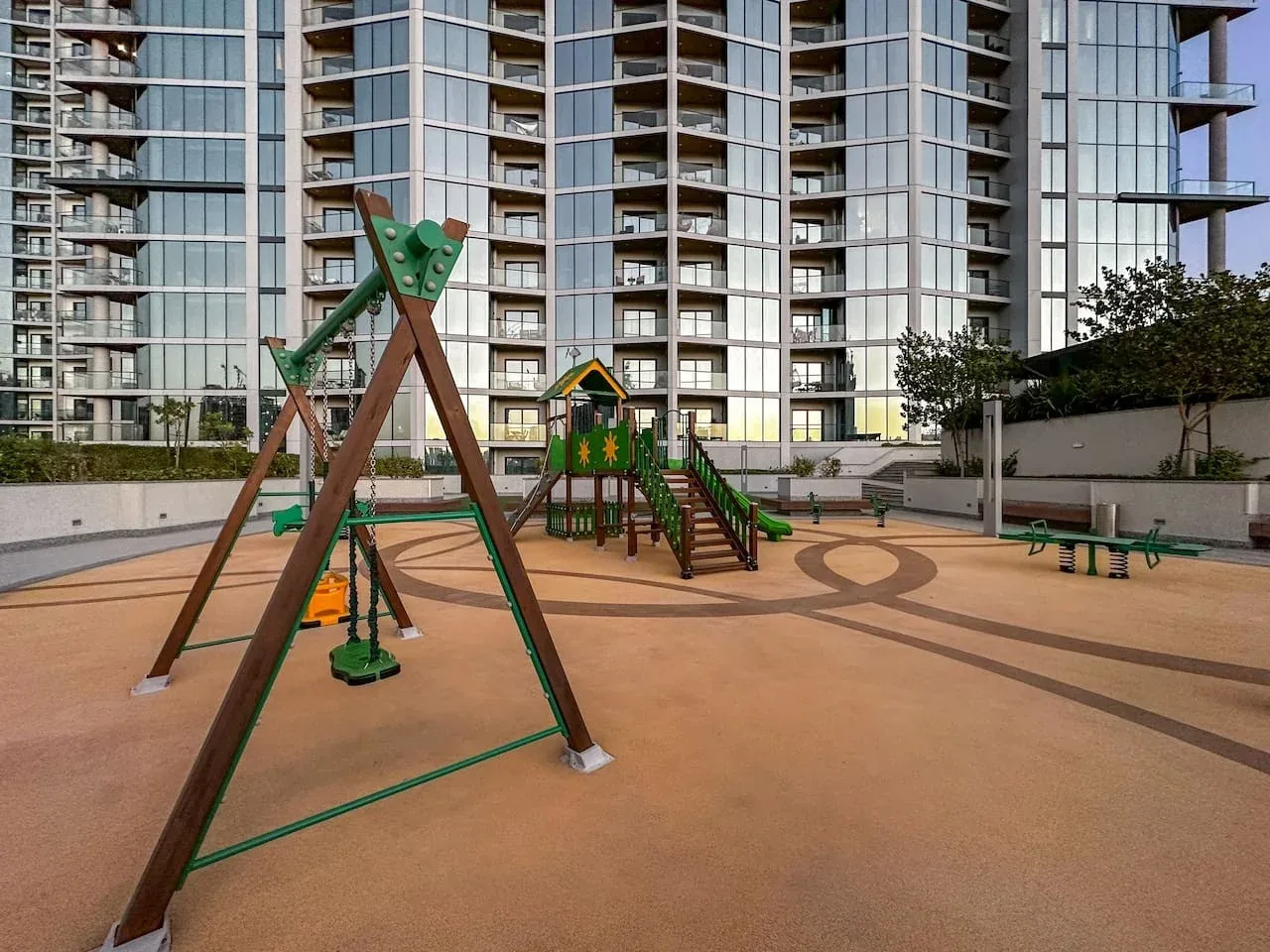 Un parque infantil al aire libre con estructuras verdes para trepar y toboganes frente a edificios de apartamentos.