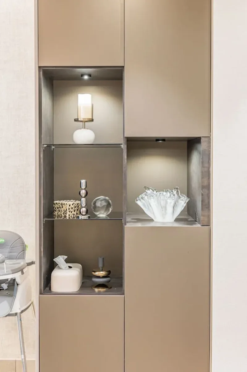 Un mueble expositor empotrado con objetos decorativos y pequeños estantes iluminados.