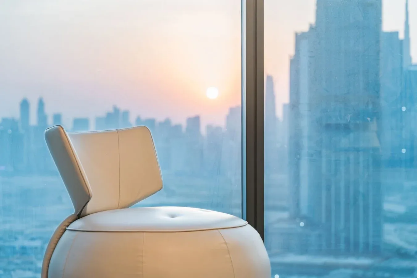 Un asiento acolchado está junto a una ventana con vistas al perfil urbano al atardecer.