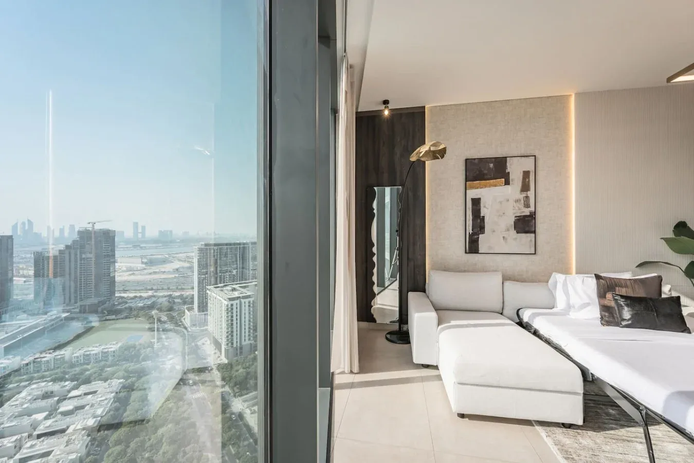 Dormitorio luminoso con cama, zona de estar y un gran ventanal con vistas a la ciudad.