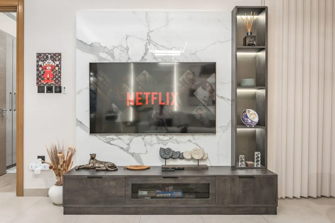 Una pared de entretenimiento en una sala de estar, con televisor, estantes y un mueble bajo.