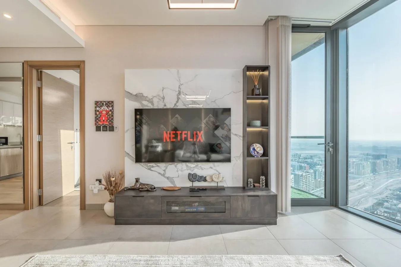 Una sala de estar con un televisor en una pared veteada junto a ventanas de piso a techo.