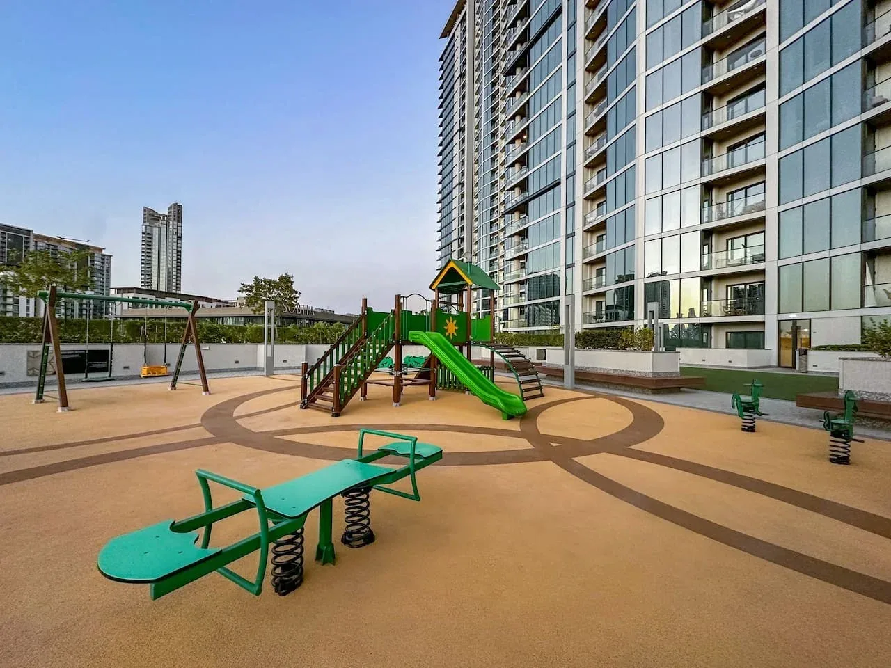 Un parque infantil junto a un edificio alto, con un tobogán verde y juegos al aire libre.
