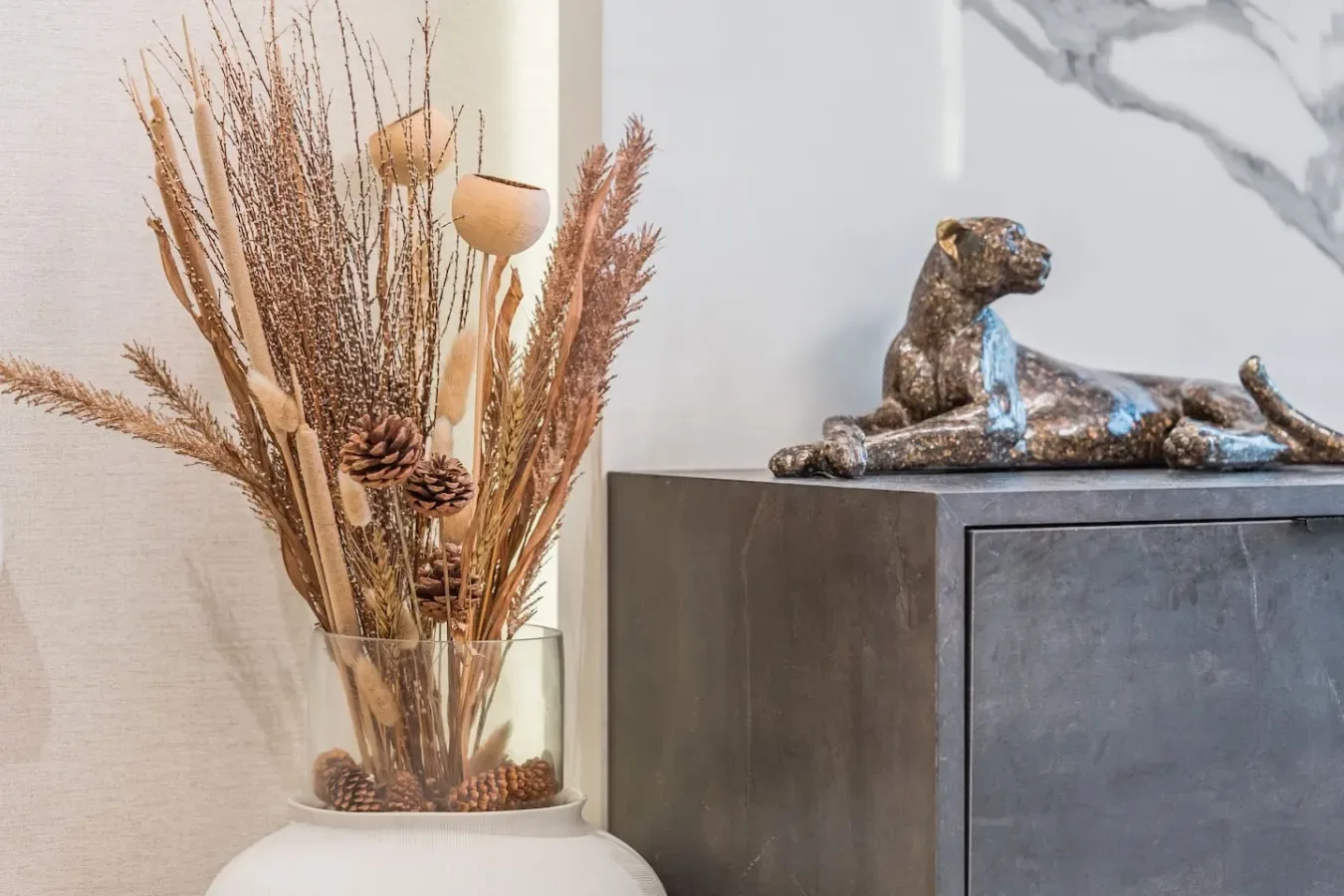 Un arreglo decorativo de hierbas secas está junto a un mueble con una pequeña escultura de un animal.