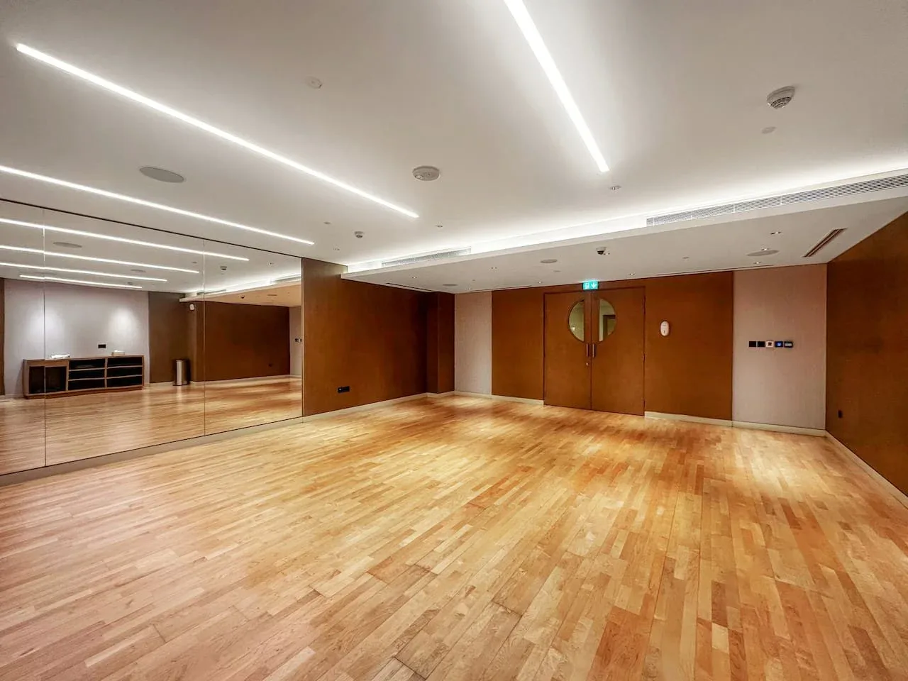 Una sala vacía con suelo de madera pulido y una pared de espejos.