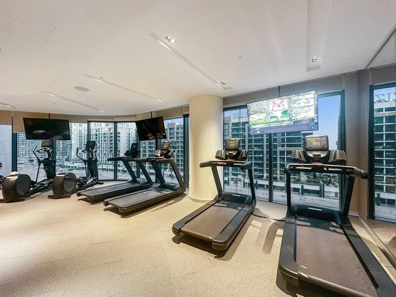Un gimnasio con cintas de correr y otros equipos de ejercicio junto a grandes ventanales.