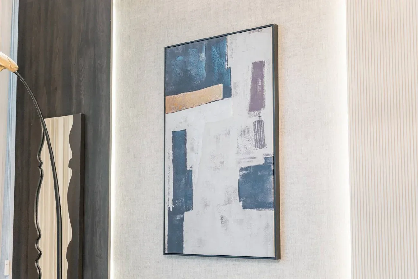 Una pintura abstracta cuelga en una pared clara junto a un panel de madera oscura.