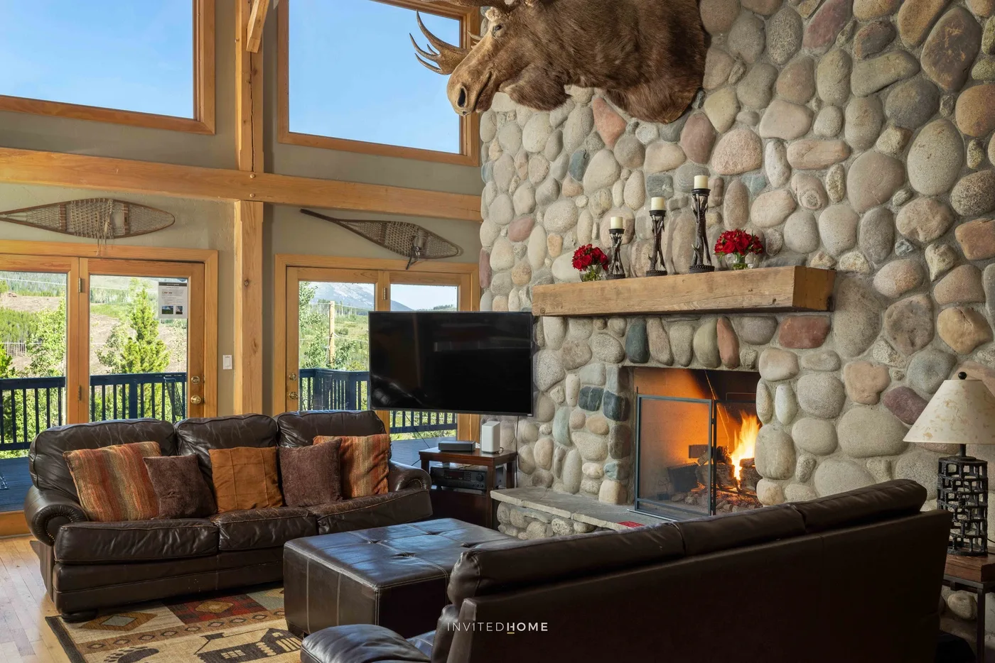 A rustic living room with leather seating, a television, and a stone fireplace.