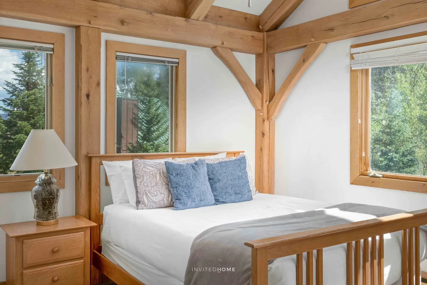 A bright bedroom with a wooden bed and large windows.