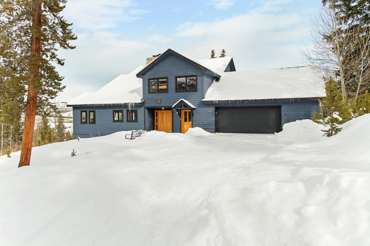 A dark blue house stands in a snowy landscape, with a garage and warm-toned entrance.
