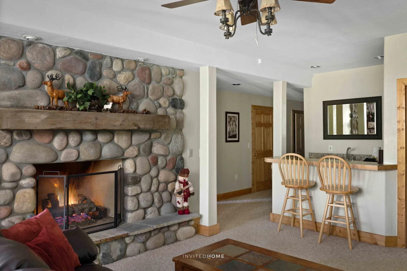 A living room with a stone fireplace and a breakfast bar with stools.