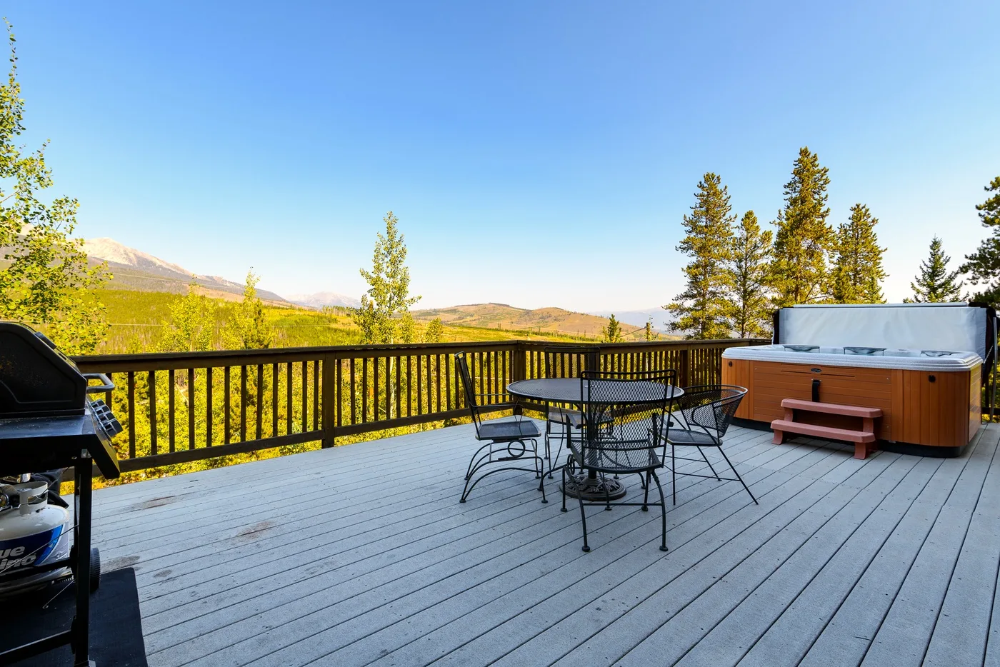 An outdoor deck overlooks a wooded landscape, with a table and hot tub.