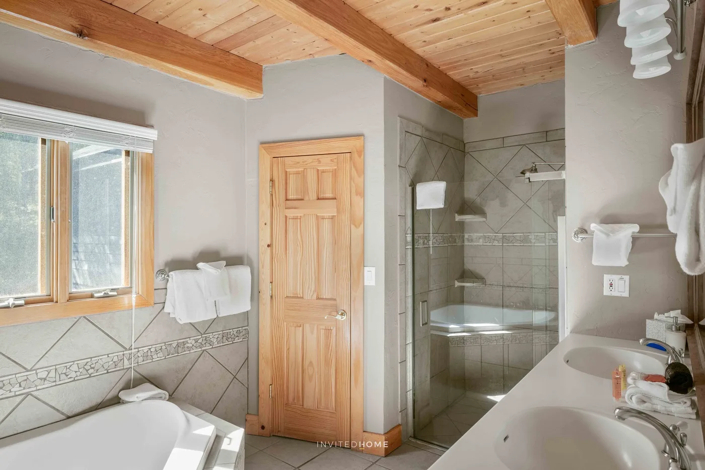 A bathroom with a wooden door, tiled shower, and sink.
