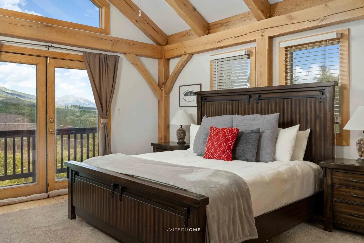 A bedroom with a large bed beneath exposed wooden beams and windows.
