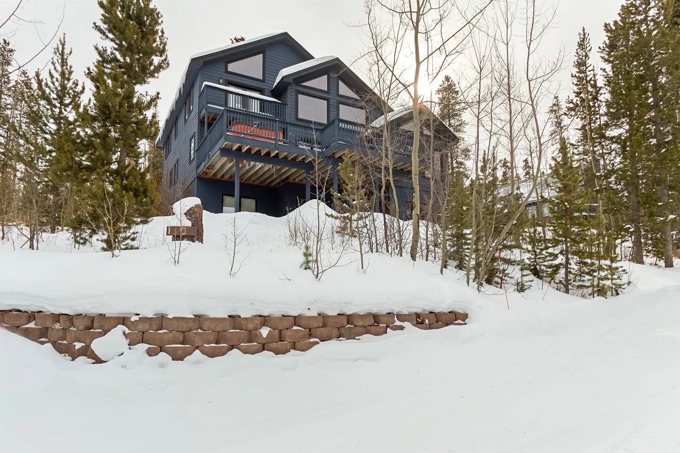 A dark blue house stands above a snow-covered slope among trees.