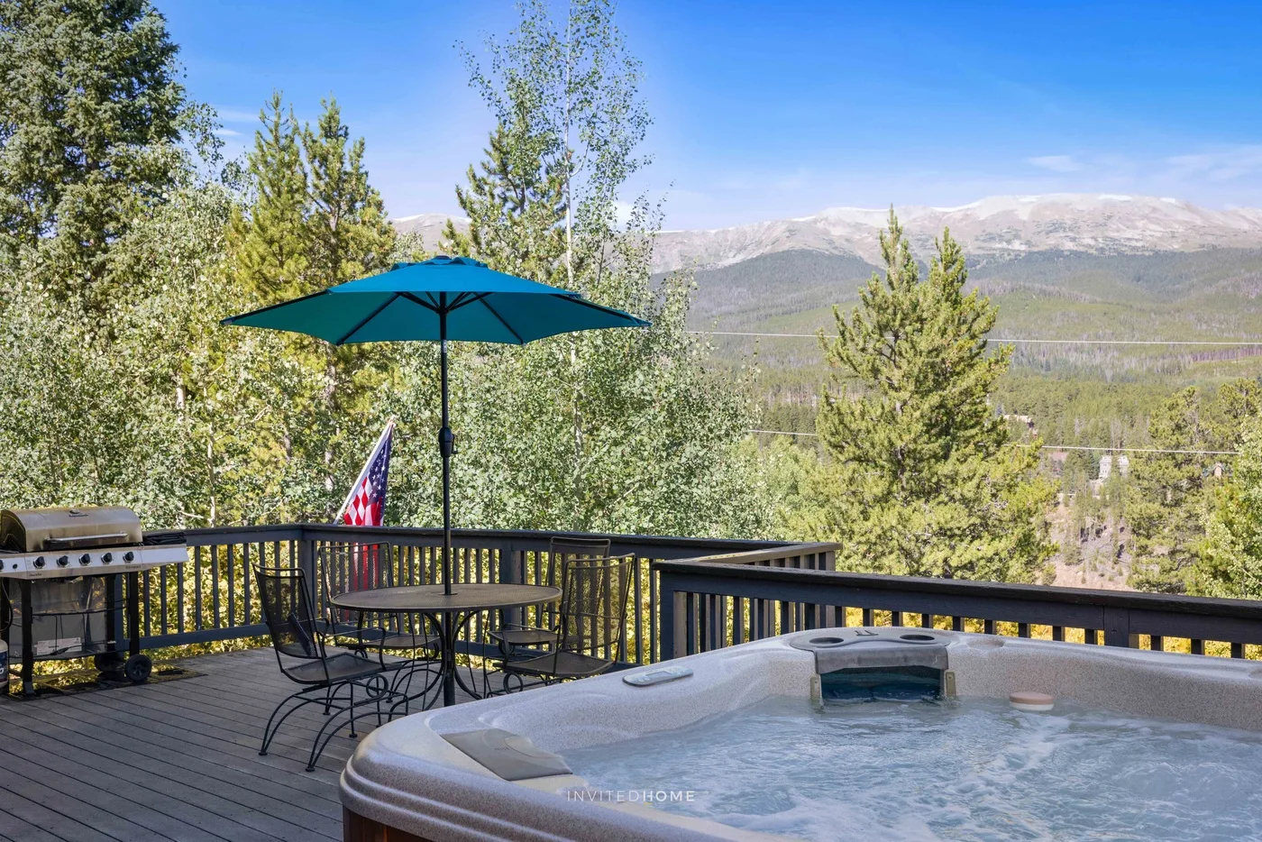 An outdoor deck overlooks a mountain landscape, with a hot tub and shaded seating.