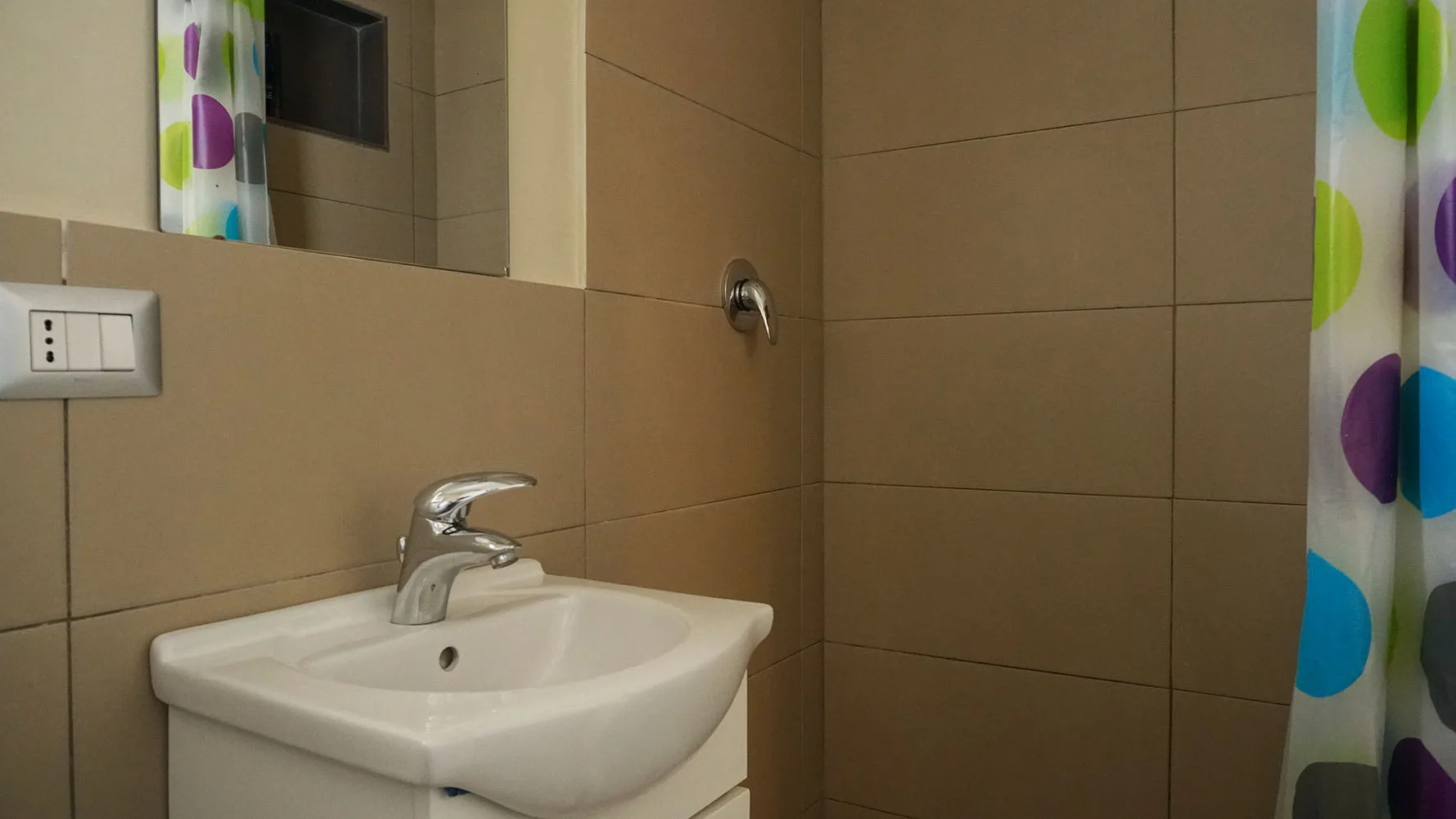 Un baño con azulejos, un lavabo blanco y una cortina de ducha colorida.