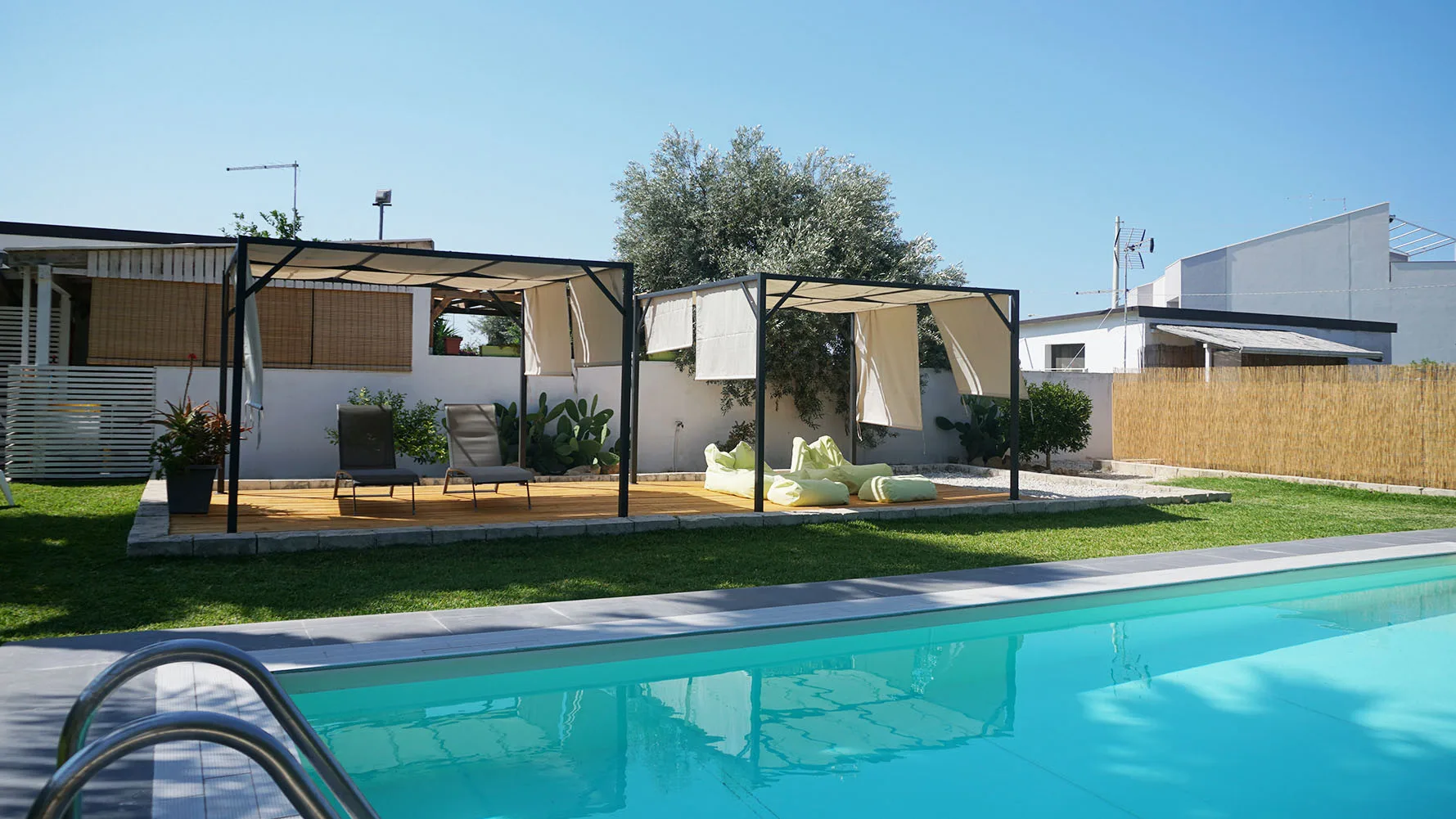 Una piscina junto a una zona de estar al aire libre con sombra y un jardín.