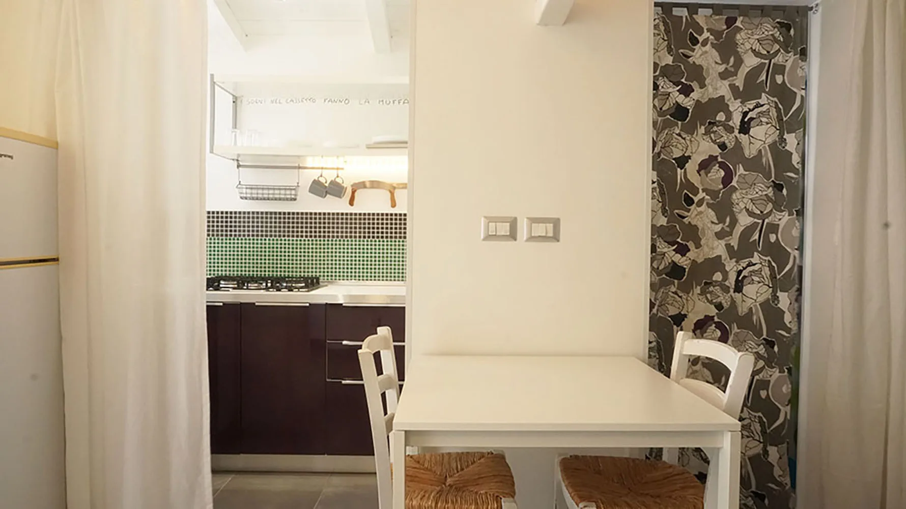 Una mesa de comedor está junto a una cocina abierta con gabinetes oscuros y una pared estampada.