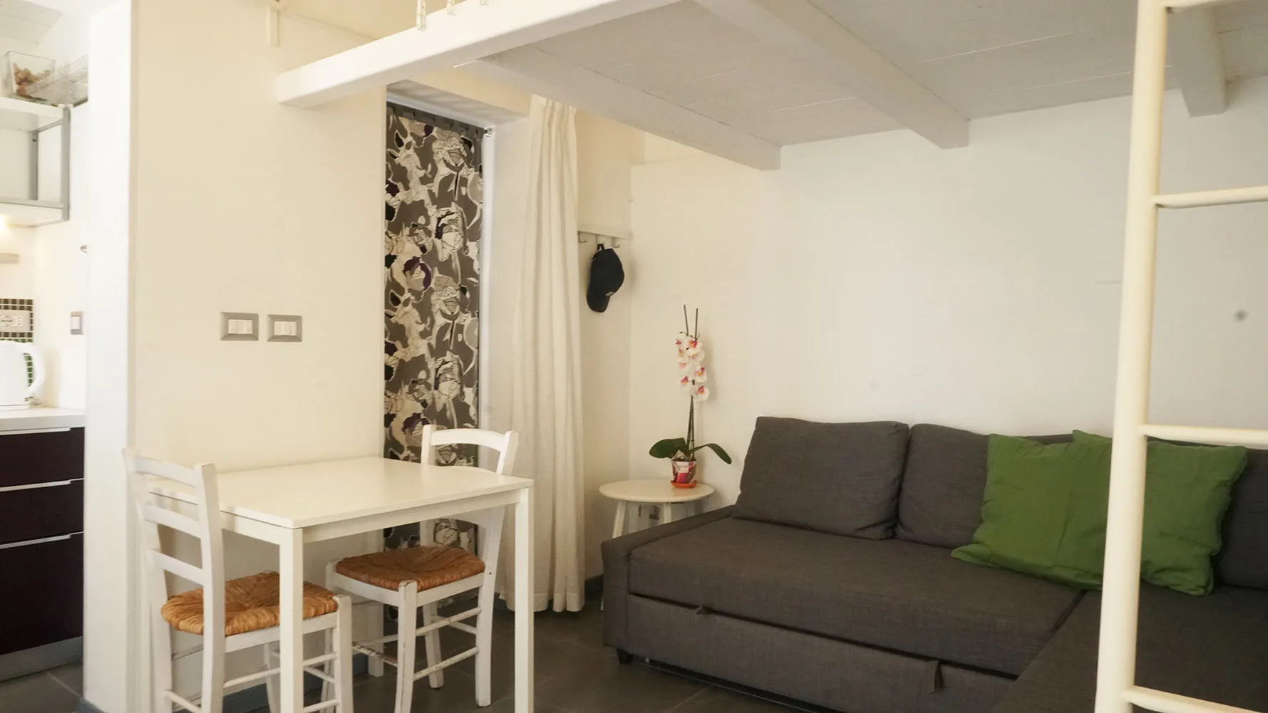 Una pequeña zona de estar y comedor con un sofá gris y una mesa blanca.
