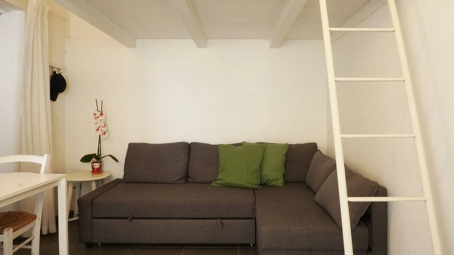 Una pequeña sala de estar con un sofá seccional oscuro y cojines verdes.