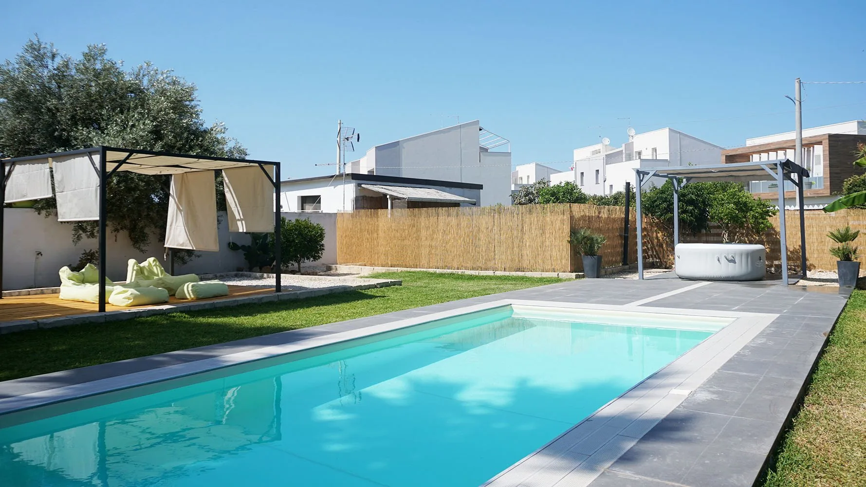 Piscina al aire libre junto a un césped, una zona de estar sombreada y una cerca de jardín.