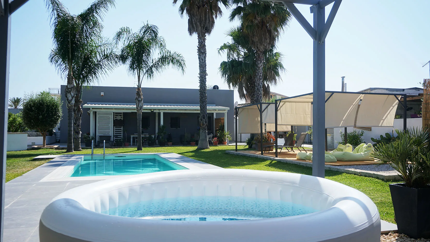 Una piscina exterior y una bañera de hidromasaje redonda están junto a un edificio bajo.