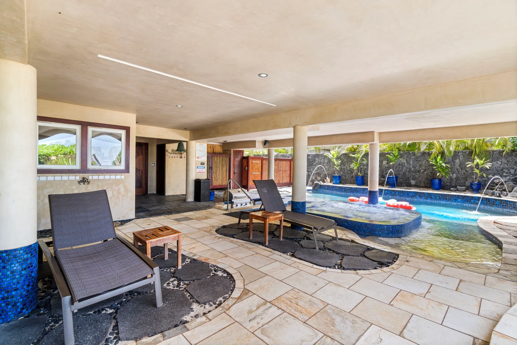 A covered poolside patio with lounge seating beside a swimming pool.
