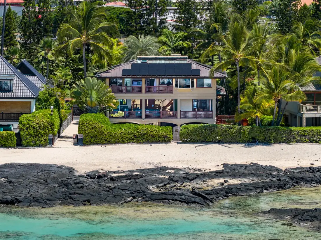 Un edificio frente a la playa se encuentra entre palmeras tropicales sobre una costa rocosa.