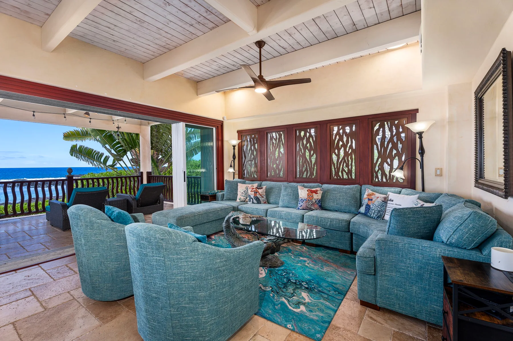 A bright living room with blue seating, a glass coffee table, and ocean views.