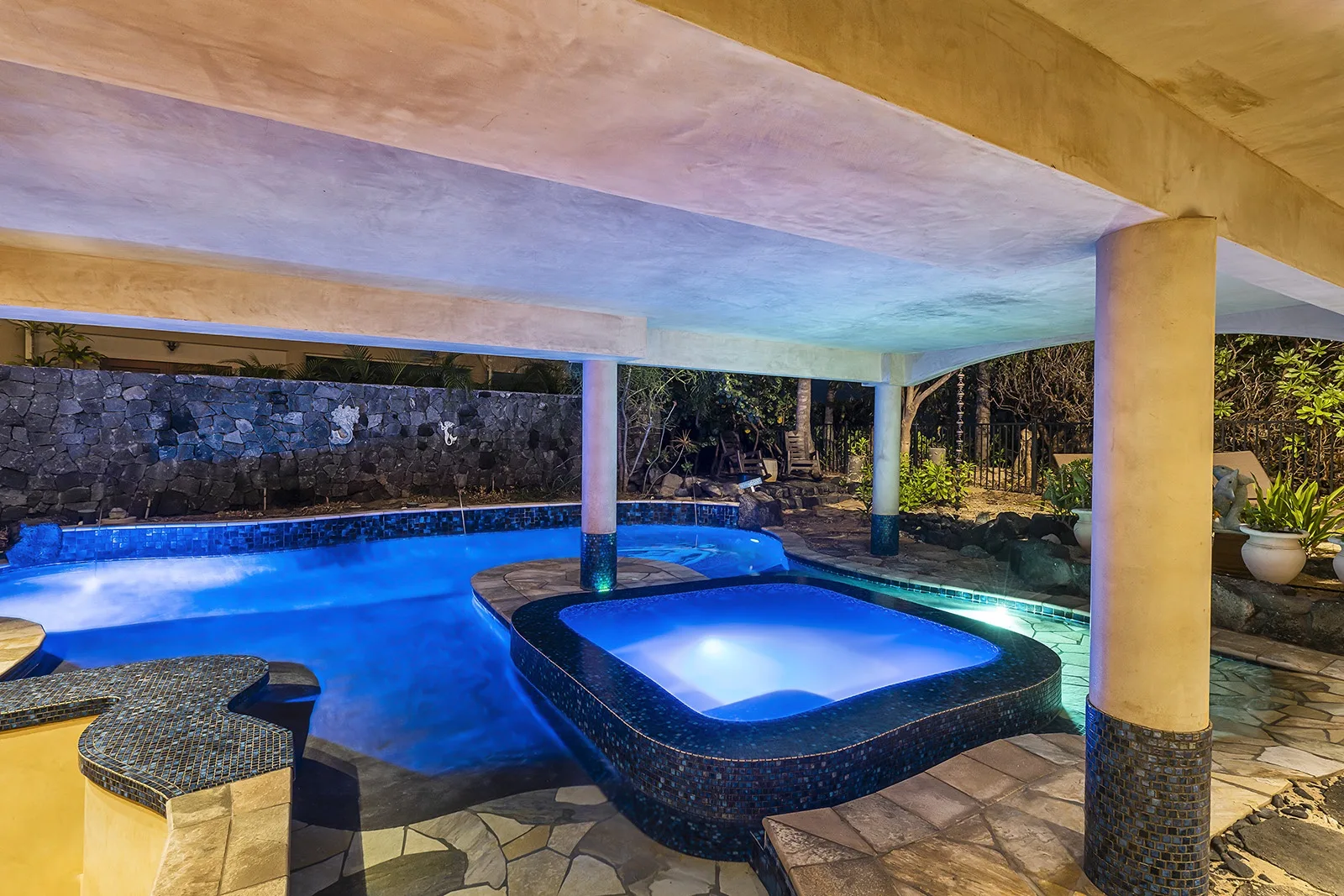 A covered outdoor pool area with a small illuminated spa beside the pool.