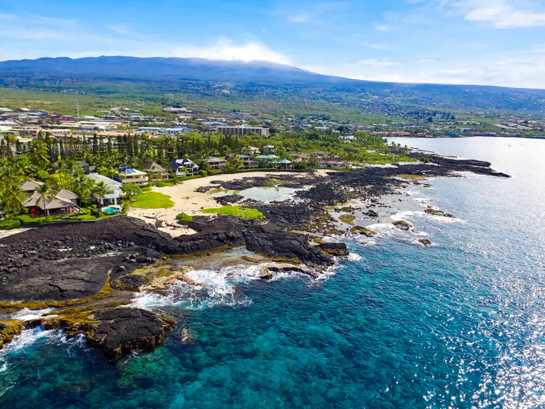 A coastal landscape with rocky shoreline, clear blue water, and greenery.