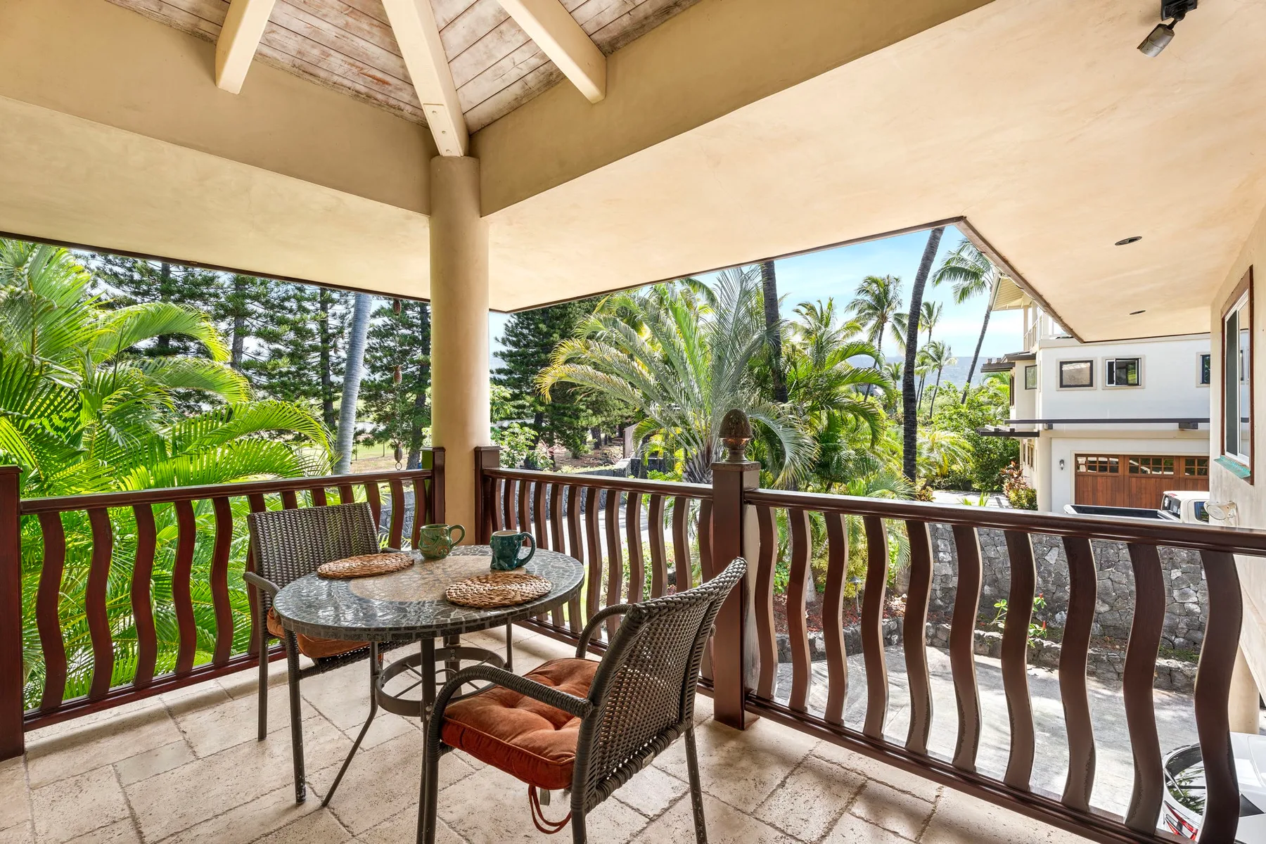 A covered outdoor balcony with seating overlooks palm trees and neighboring buildings.