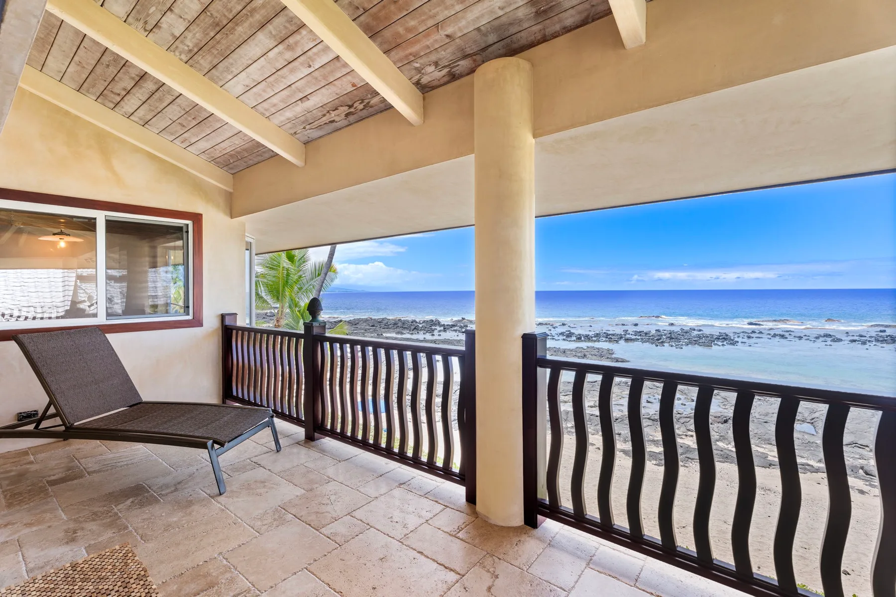 A covered balcony overlooks the ocean, with tiled flooring and a dark railing.