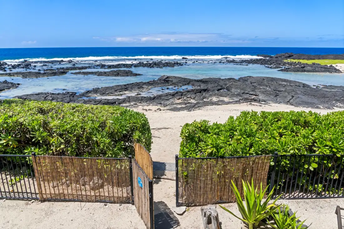 A sandy beach with rocky tide pools and ocean waves beyond the shore.