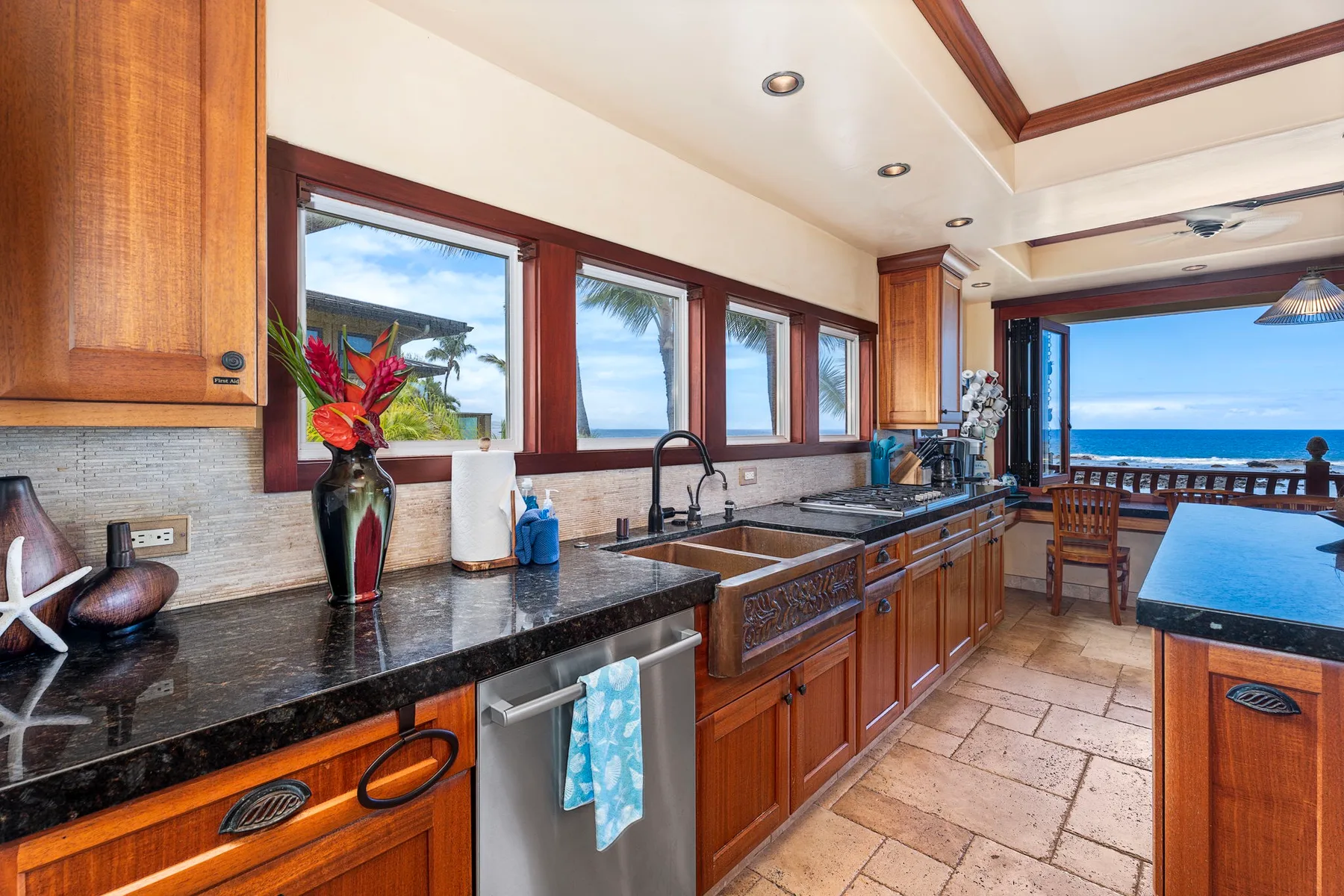 A spacious kitchen with wooden cabinets, dark countertops, and windows overlooking the water.