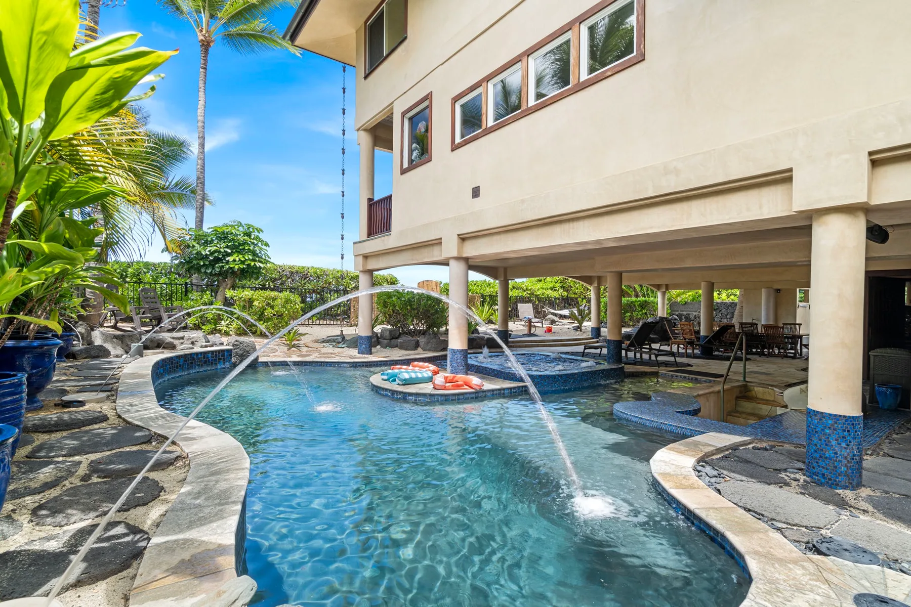 An outdoor swimming pool curves beside a building, with water arches spraying into it.