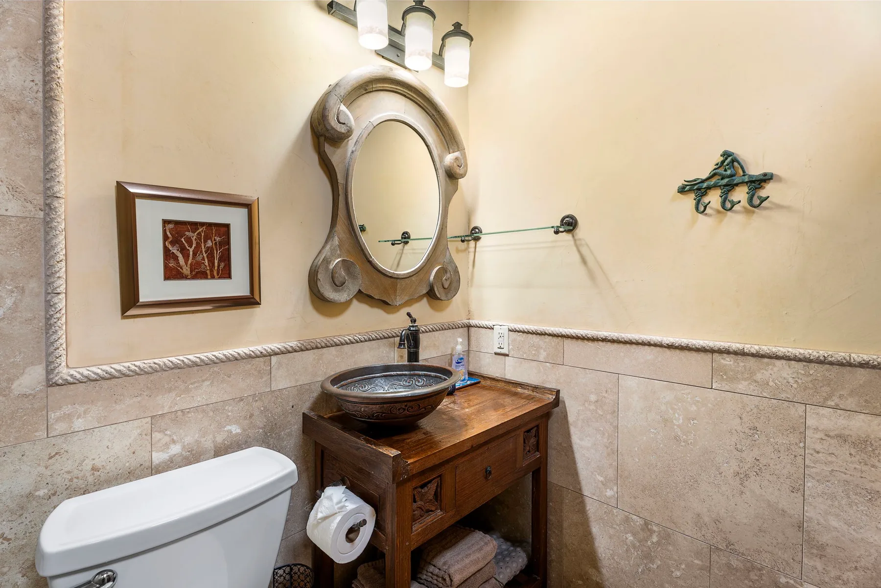 A bathroom vanity with an oval mirror, framed picture, and tiled walls.