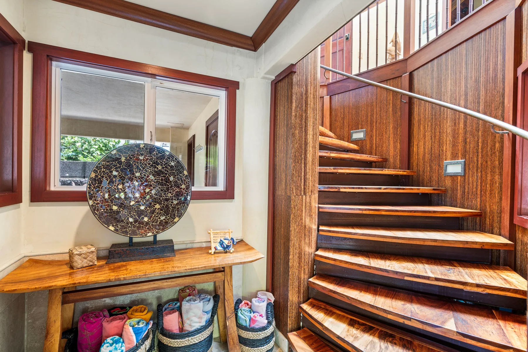 A wooden staircase rises beside a console table and decorative lamp.