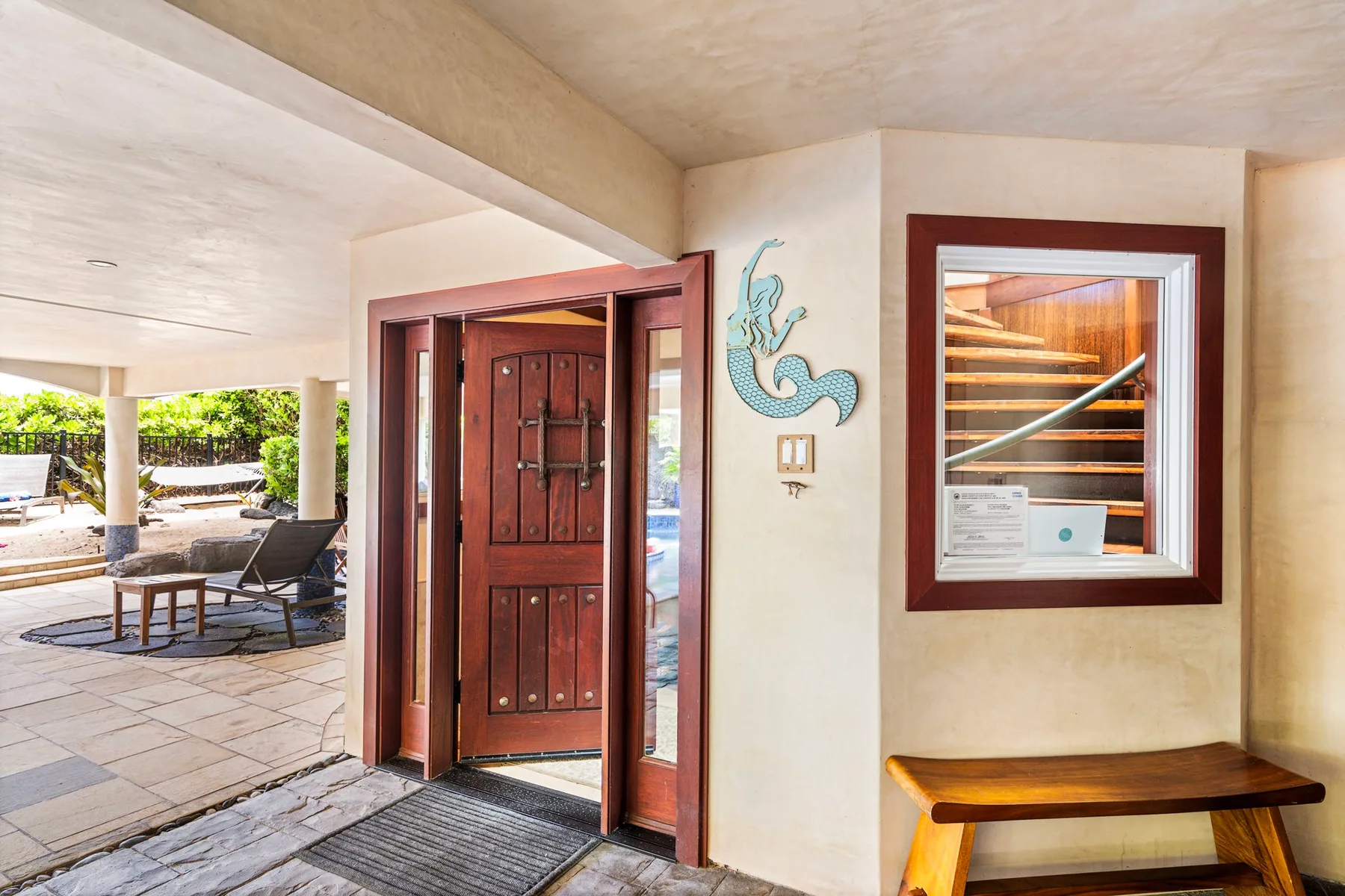 A covered patio entrance with an open wooden door and a bench.