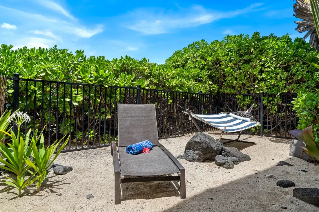 A sunny outdoor patio with a lounge chair and hammock beside lush greenery.