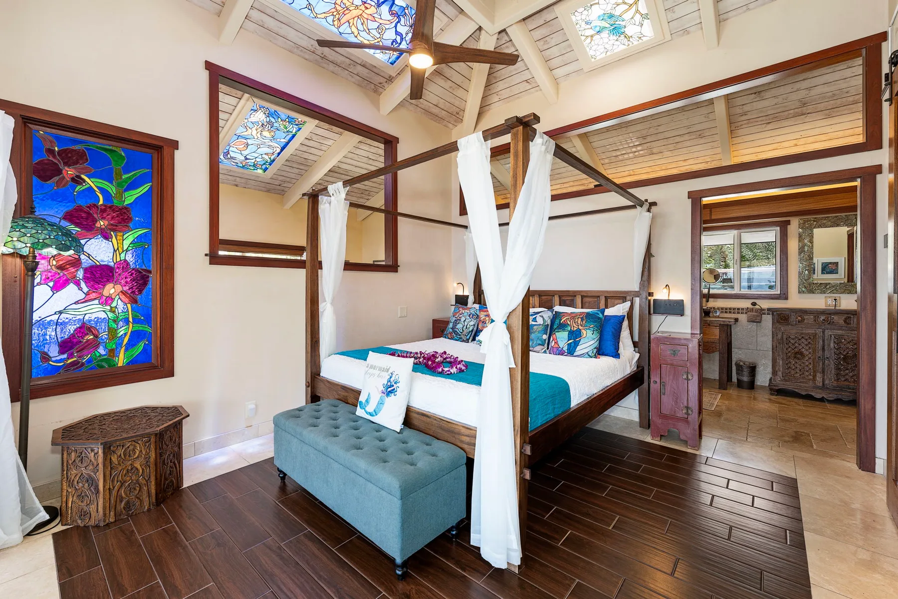 A bedroom with a canopy bed, colorful glass panels, and an adjoining bathroom.