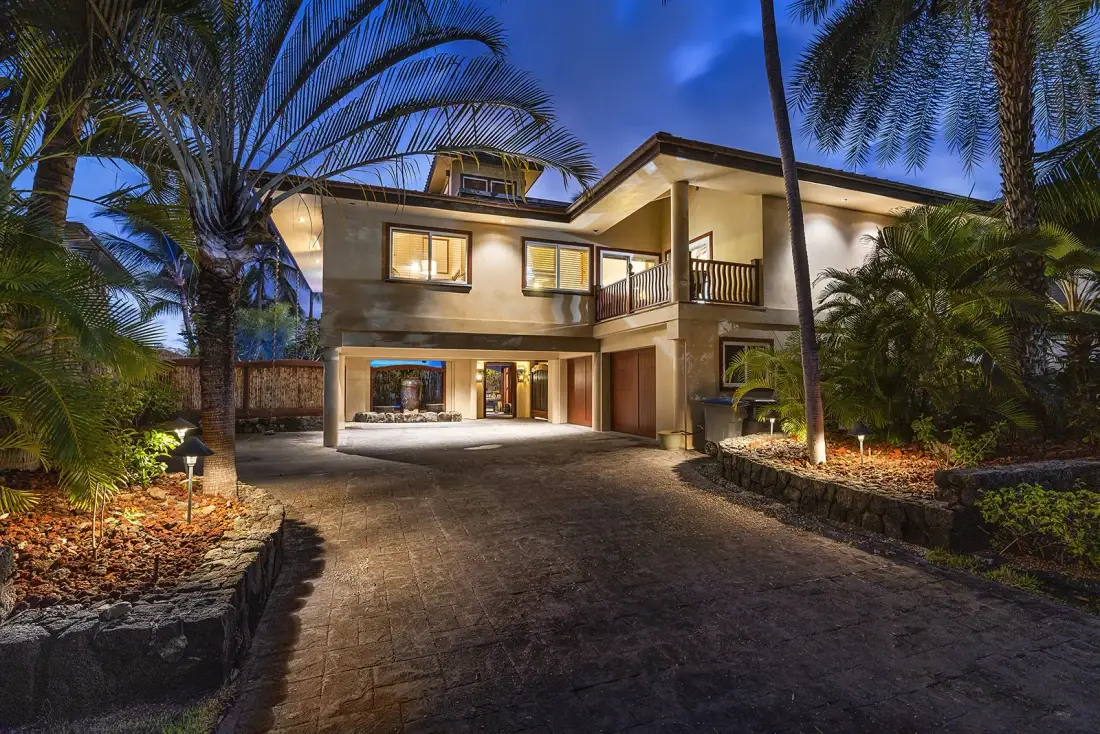 A modern two-story house is lit at night, with a paved driveway in front.